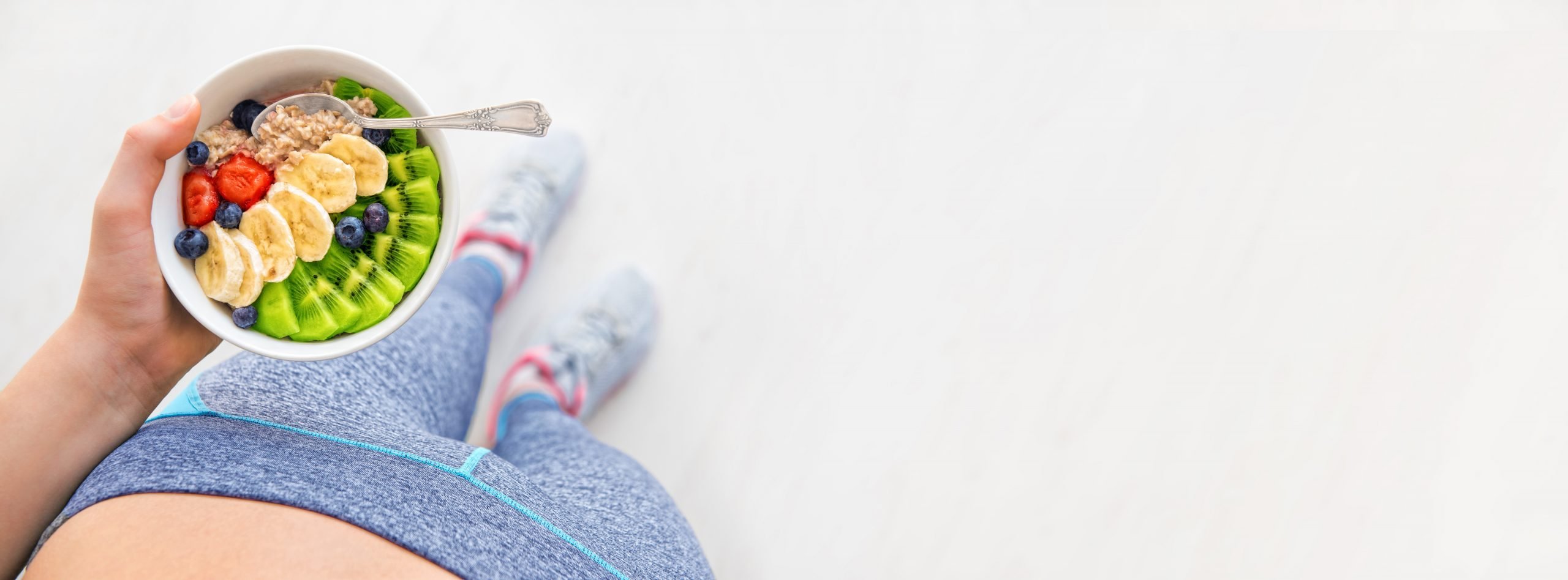 Young woman is resting and eating a healthy oatmeal after a workout.