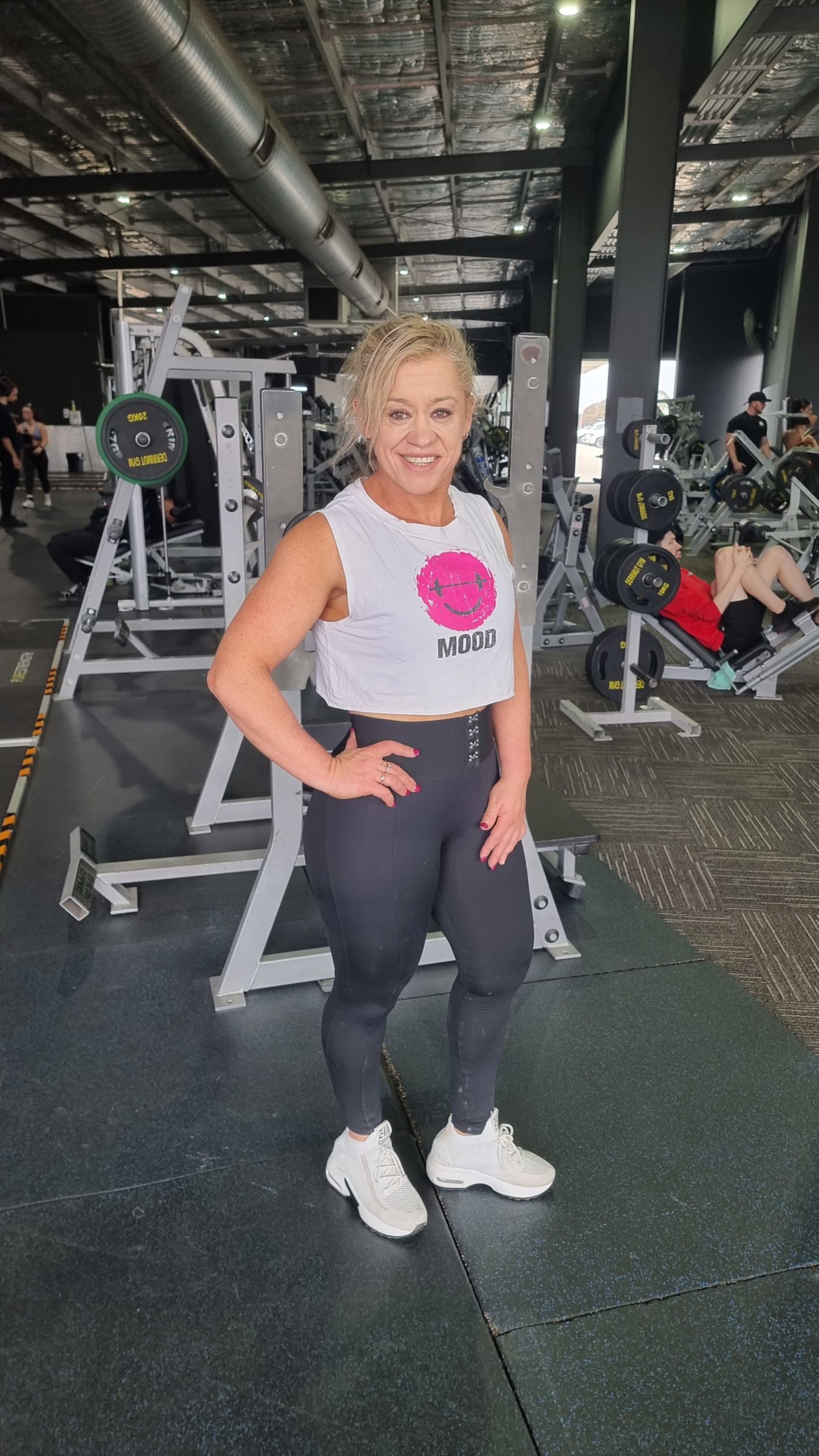 Girl standing in gym in black leggings and white singlet